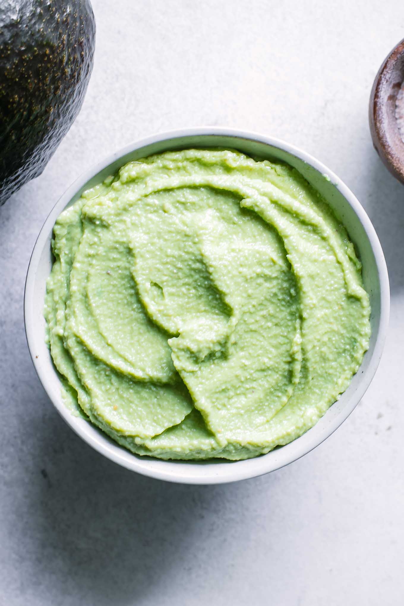 a bowl of green avocado and cashew sauce on a white table