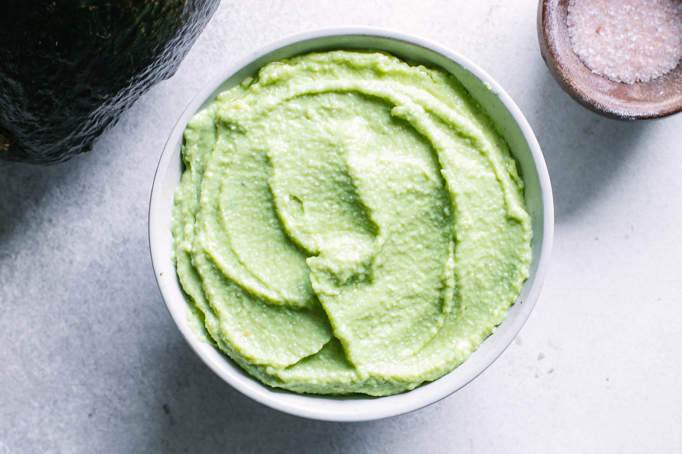 a bowl of vegan avocado crema sauce on a white table with an avocado