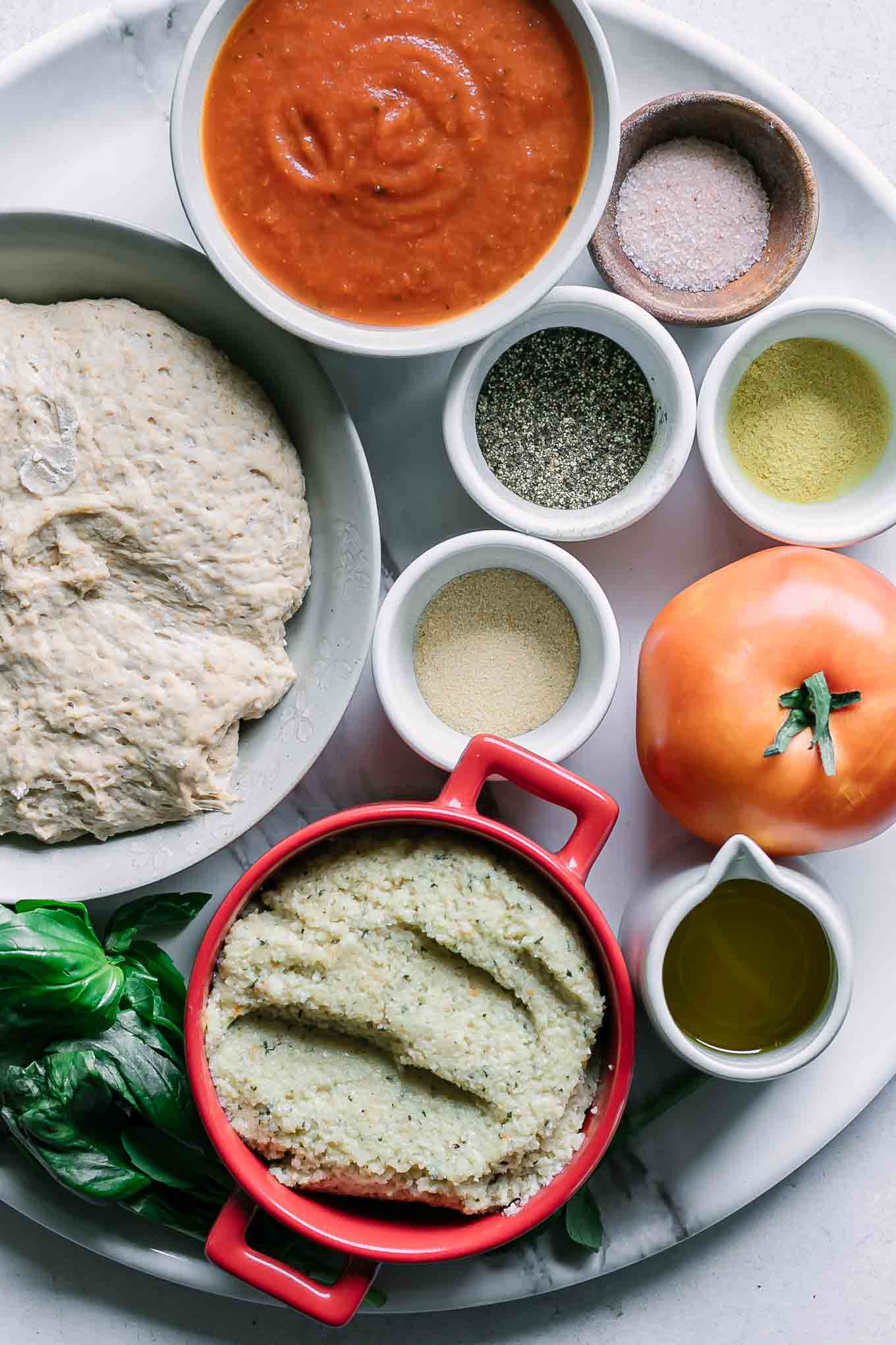 pizza dough, tomato, fresh basil, and bowls of marinara sauce, oil, salt, pepper, and seasonings for vegan margherita pizza