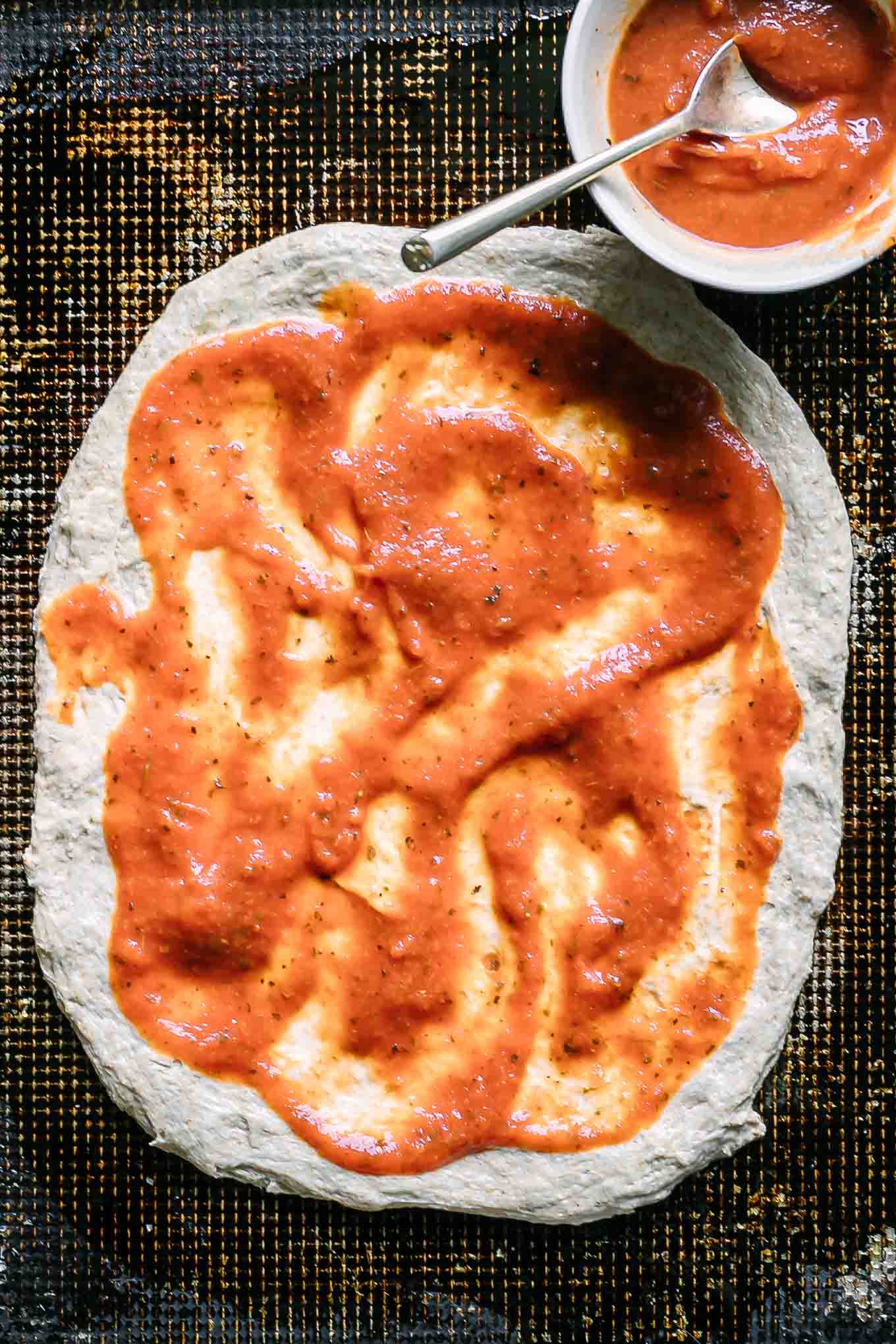 marinara sauce spread on top of pizza dough on a baking sheet