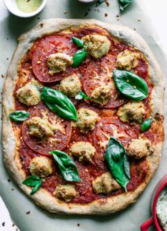 a vegan margherita pizza on a table with fresh basil, mozzarella, and tomatoes
