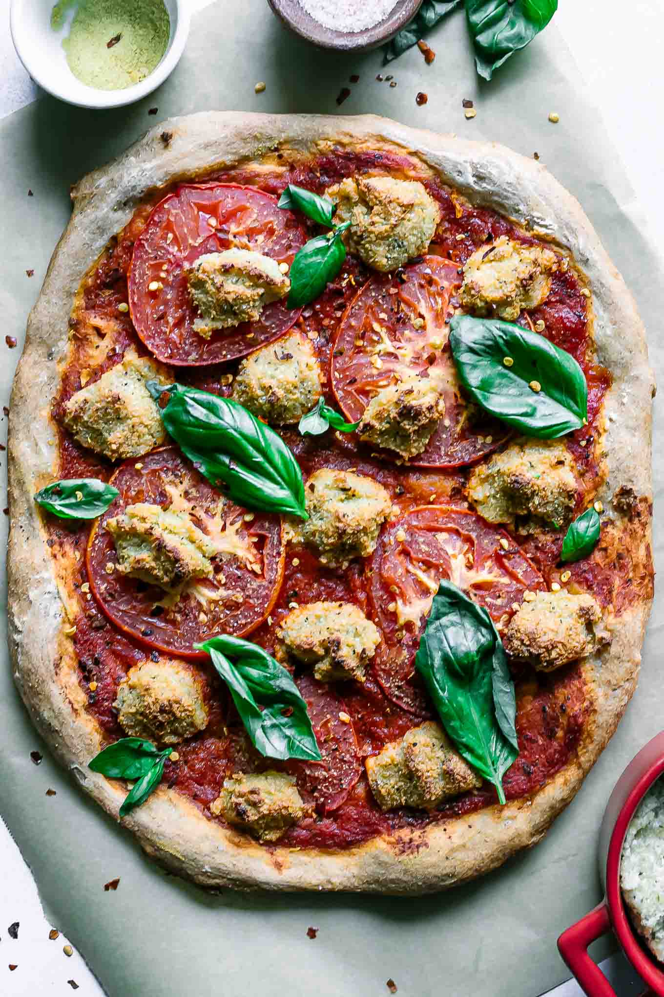 a vegan margherita pizza on a table with fresh basil, mozzarella, and tomatoes