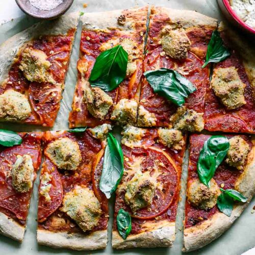 a vegan margherita pizza with sliced tomatoes, vegan mozzarella cheese, and fresh basil on a white table