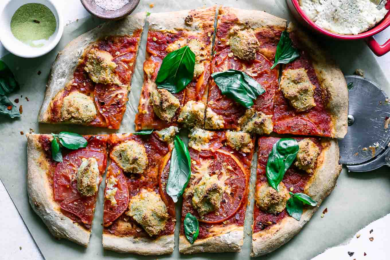 a vegan margherita pizza with sliced tomatoes, vegan mozzarella cheese, and fresh basil on a white table