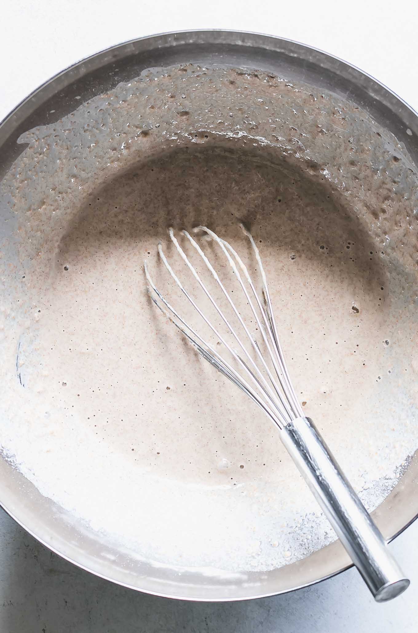 a mixing bowl with pancake batter and a whisk on a white table