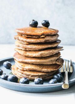 a stack of vegan whole wheat pancakes on a blue plate with blueberries on a white table