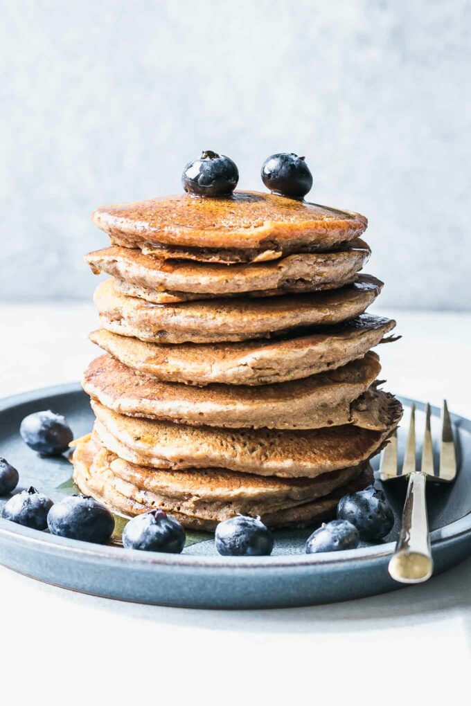 a stack of vegan whole wheat pancakes on a blue plate with blueberries on a white table