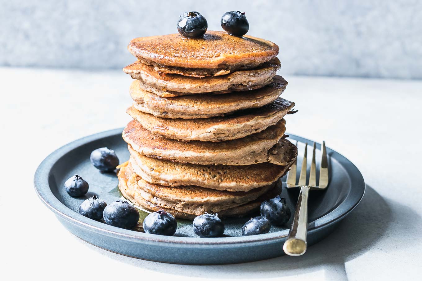 a stack of whole wheat pancakes on a blue plate with maple syrup and blueberries
