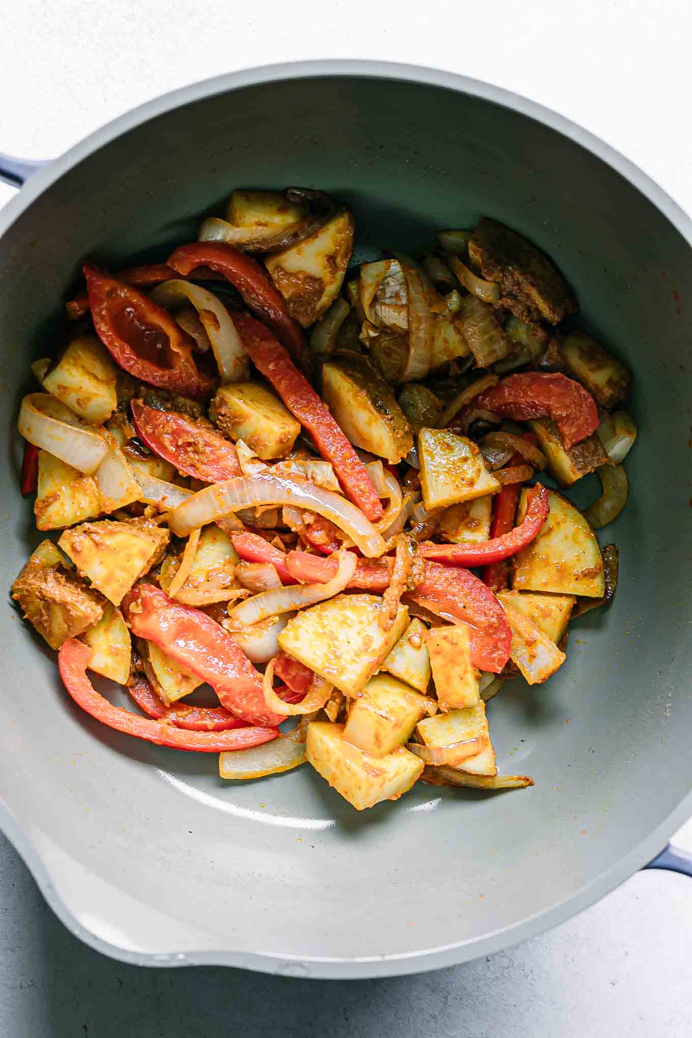 cooked onion, bell peppers, and potatoes with yellow curry paste in a pot