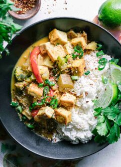 a black bowl with yellow curry and tofu with white rice on a white table