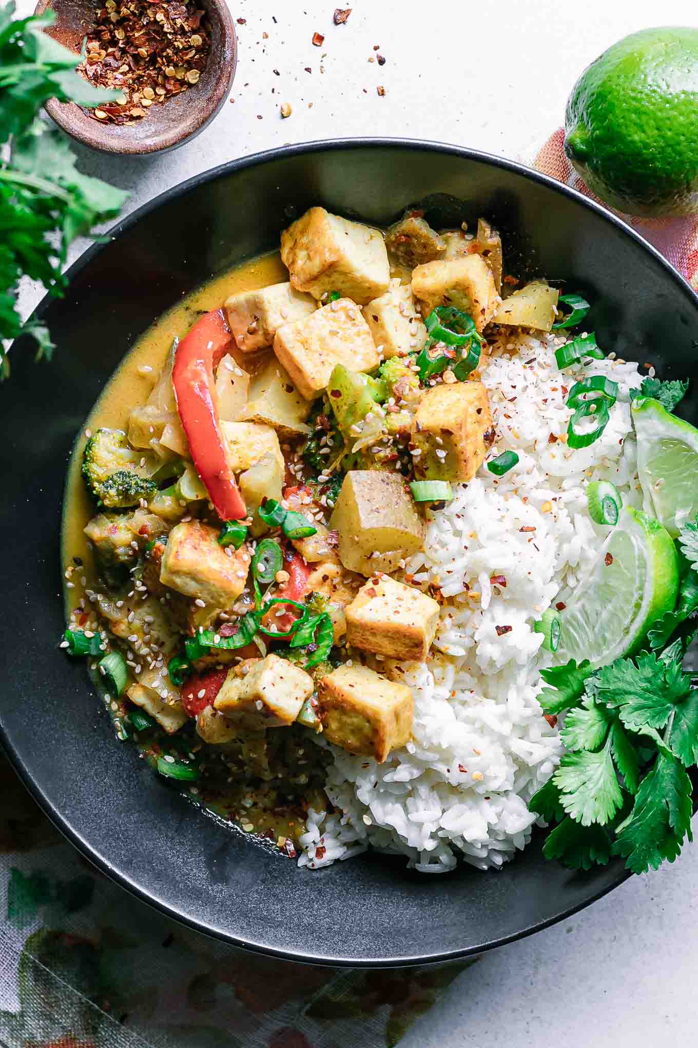 a black bowl with yellow curry and tofu with white rice on a white table