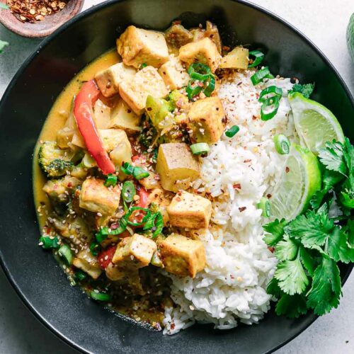 a yellow curry tofu bowl with white rice on a white table