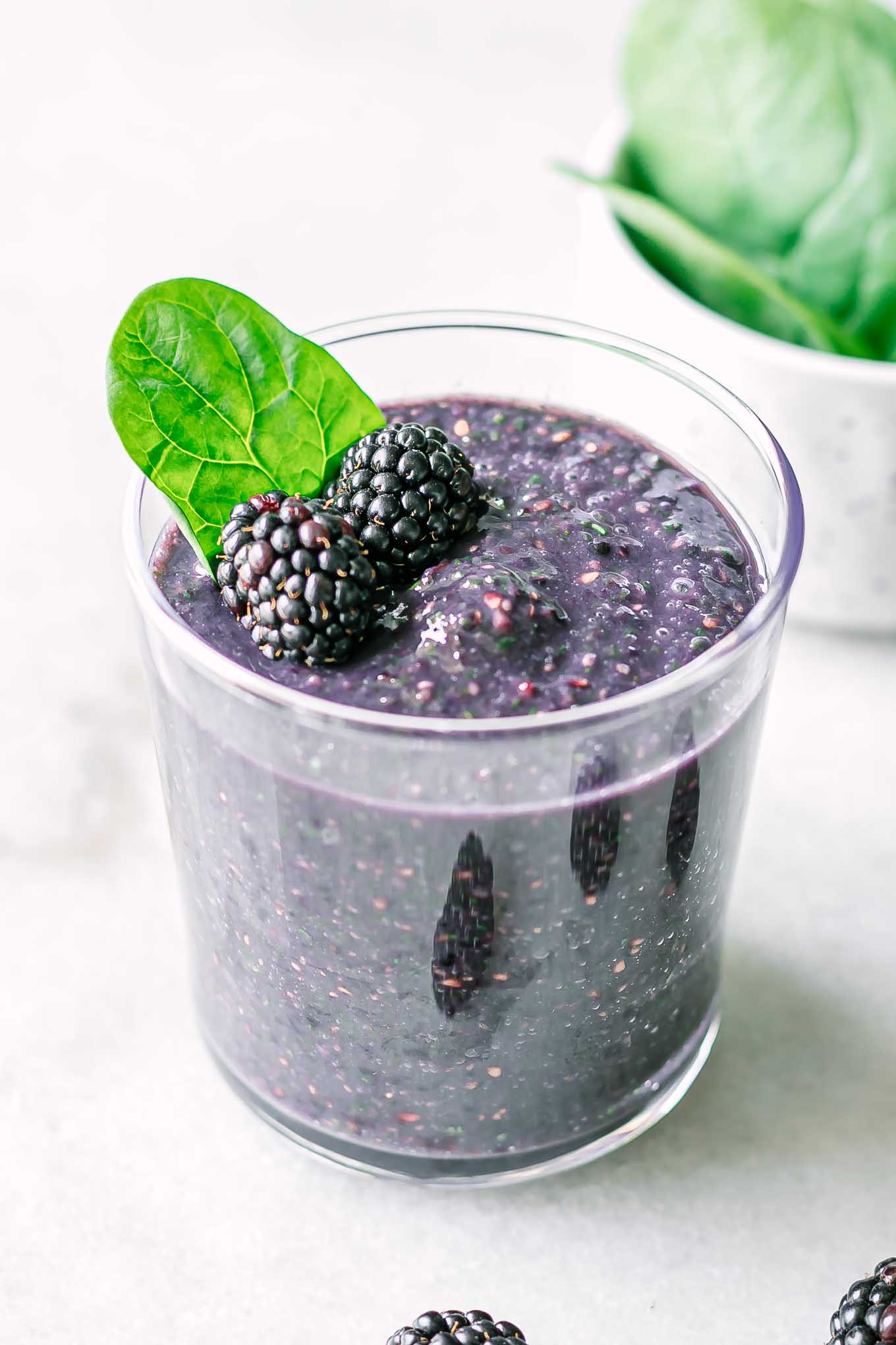 a glass of blackberry spinach smoothie with a spinach garnish on a white table
