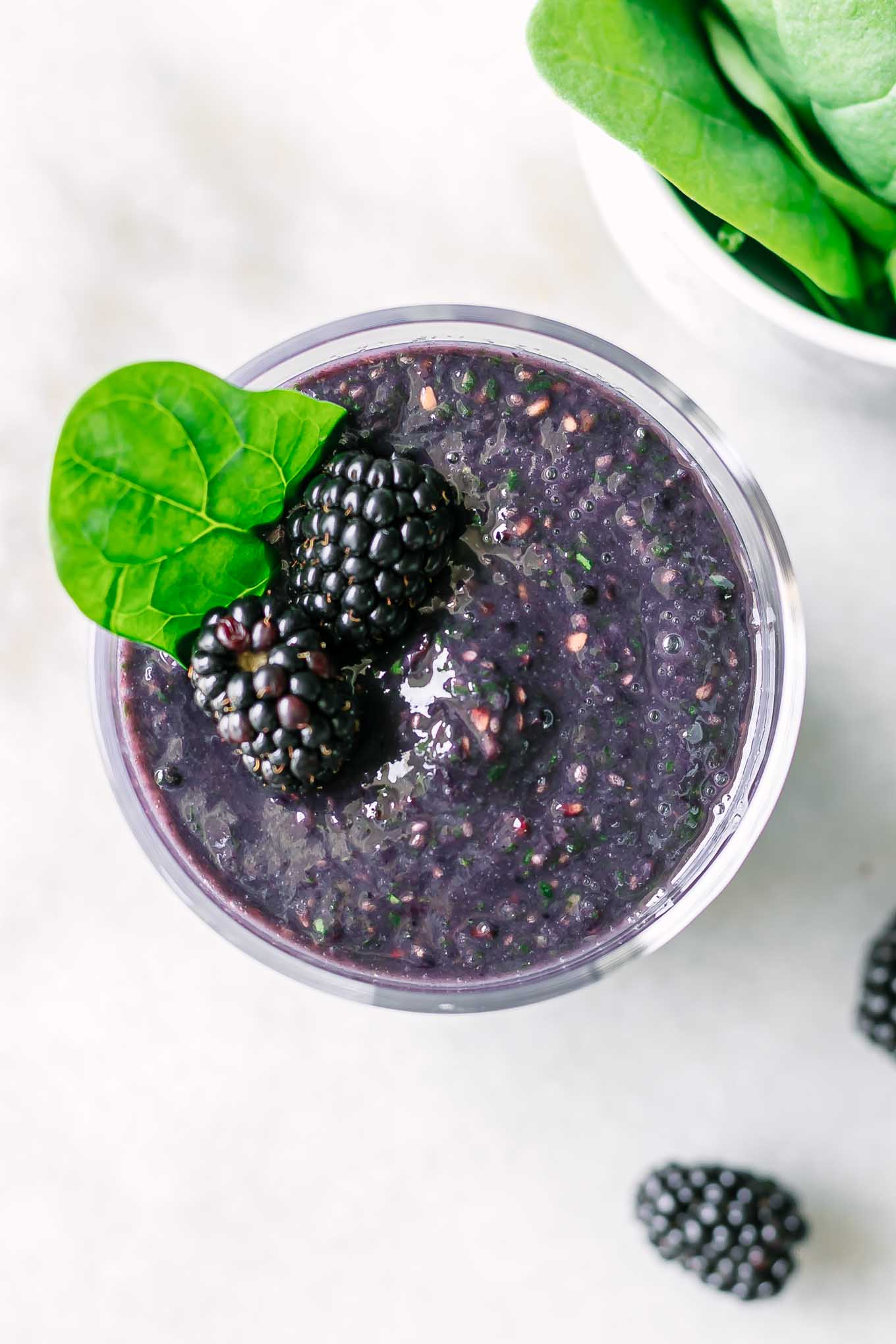 a close up photo of the top of a blackberry spinach smoothie on a white table