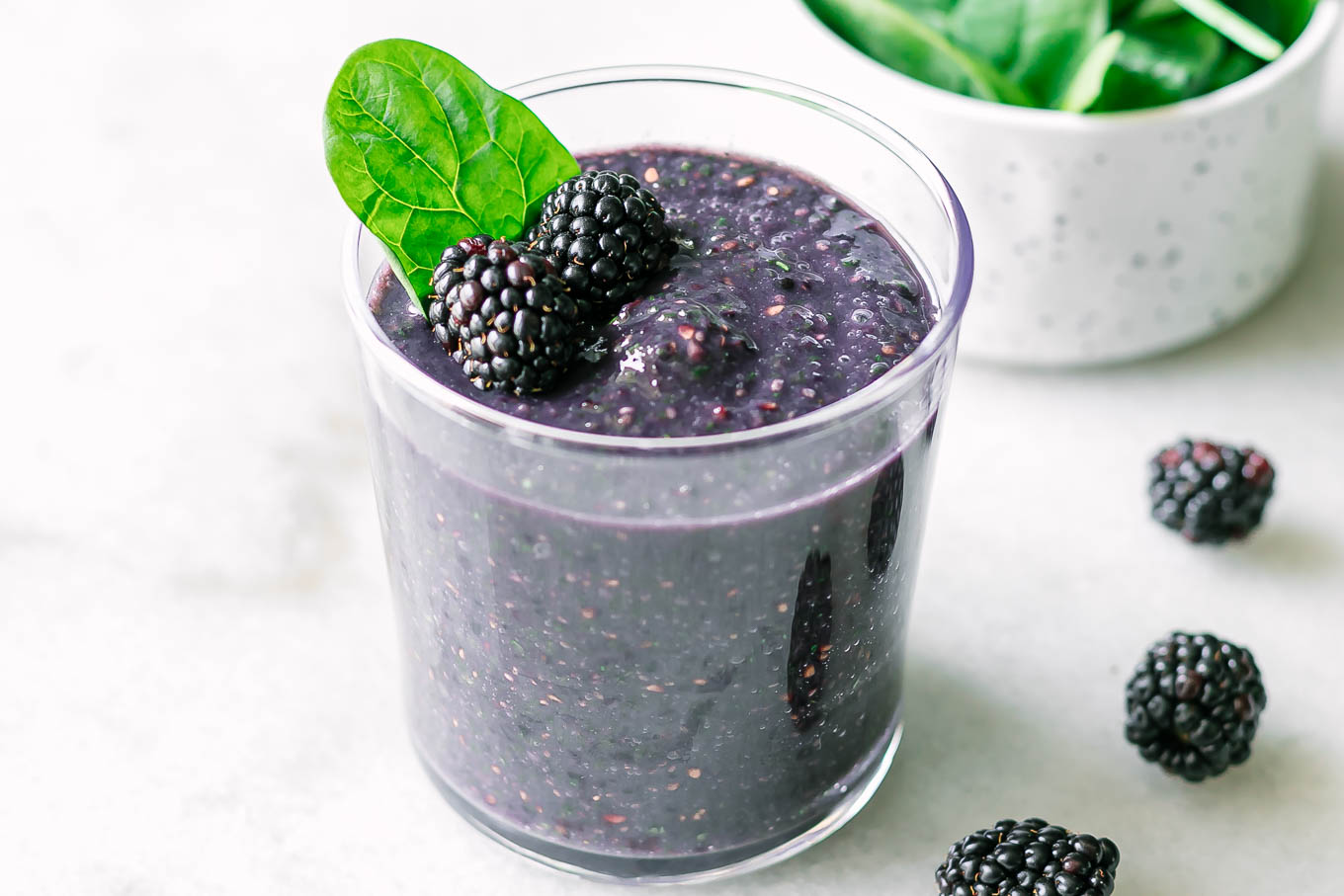 a spinach blackberry smoothie in a glass on a white table with fresh blackberries
