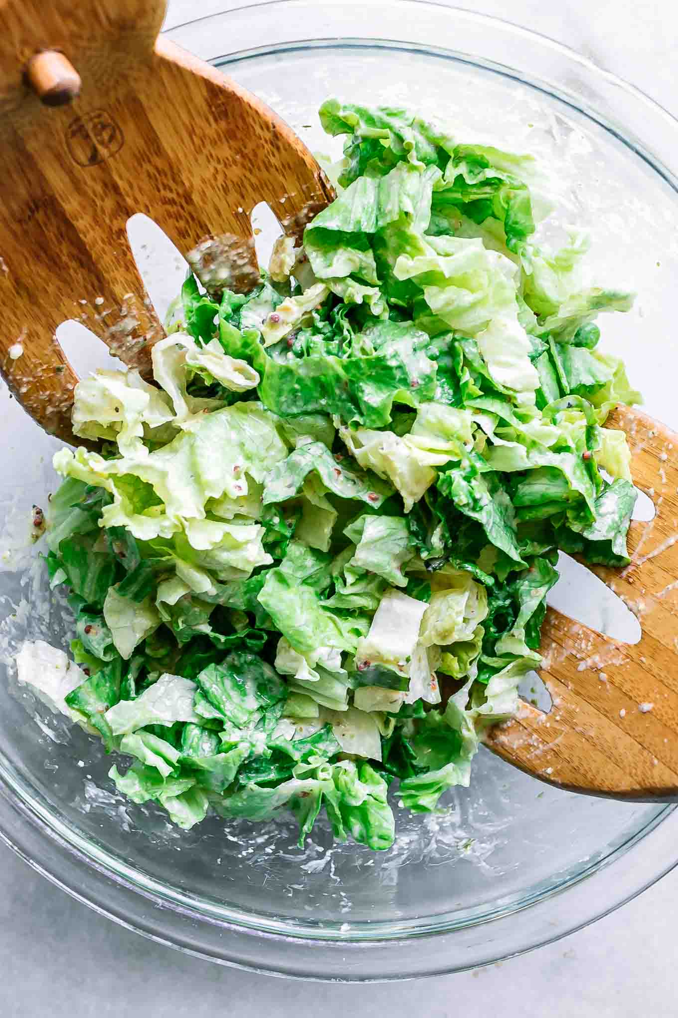 a bowl with cut romaine lettuce with caesar dressing with salad tongs