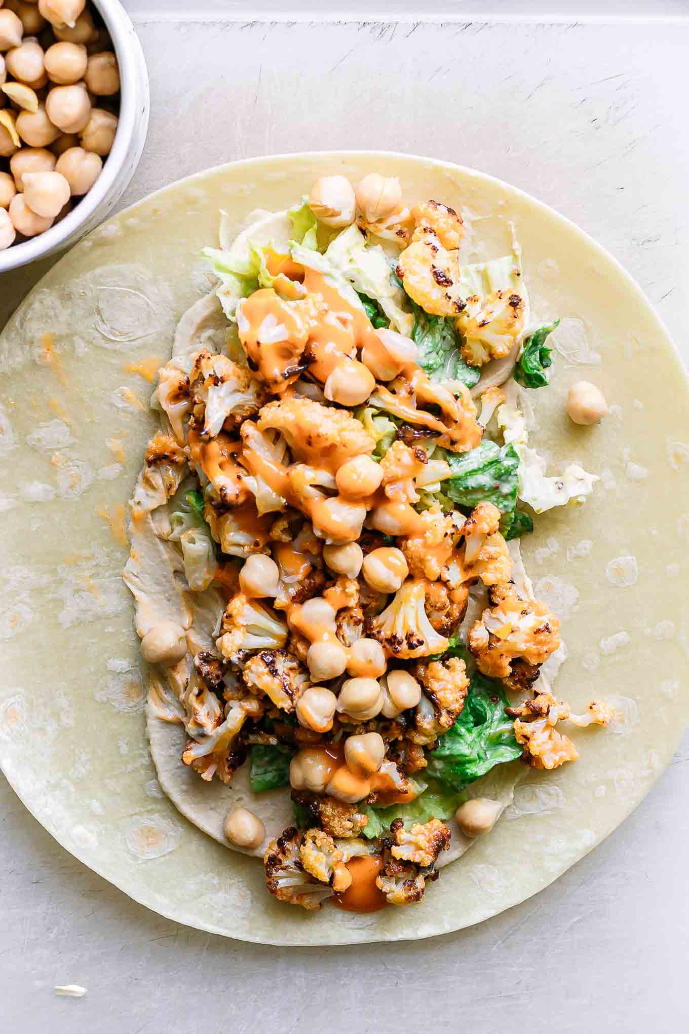 a tortilla with buffalo cauliflower wrap ingredients on a white table