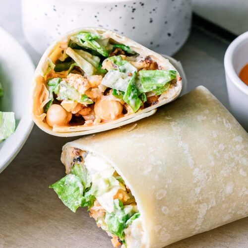 cut buffalo cauliflower wrap halves on a table with bowls of ingredients