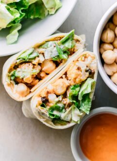 cut buffalo cauliflower wrap halves on a table with bowls of ingredients