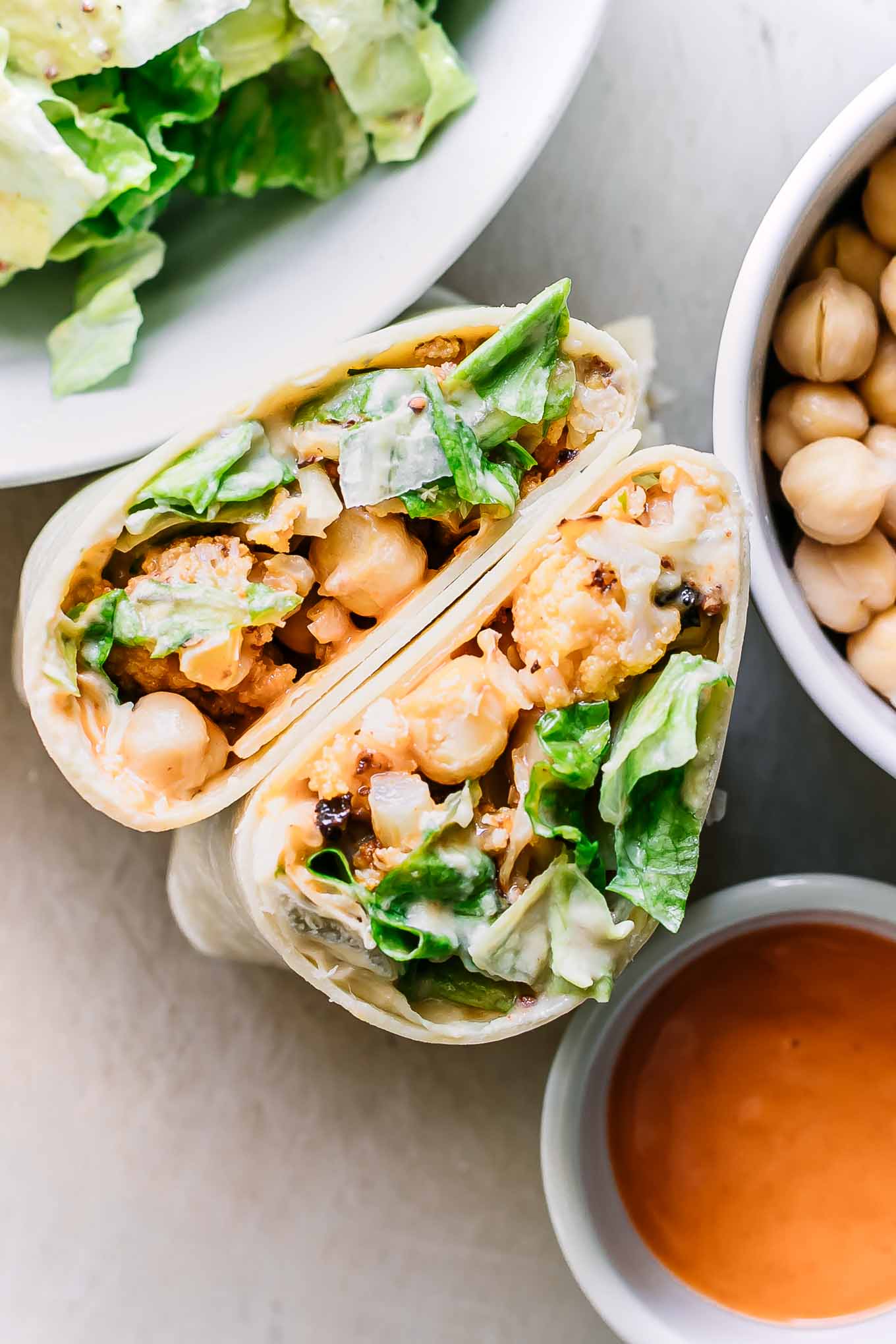 cut buffalo cauliflower wrap halves on a table with bowls of ingredients