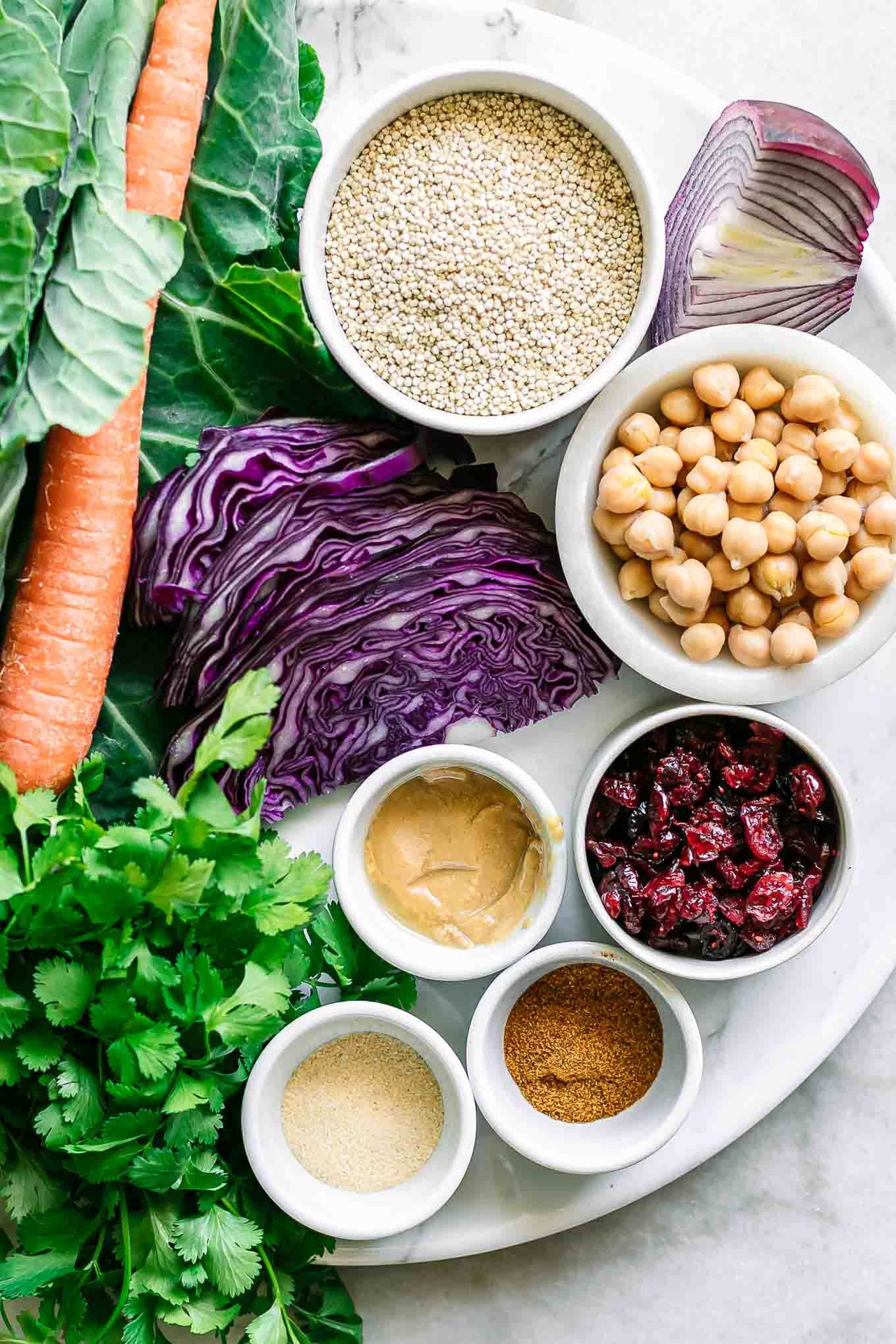 collard greens, chickpeas, quinoa, cilantro, cabbage, onion, and bowls of spices and sauce ingredients for collard wraps on a white table