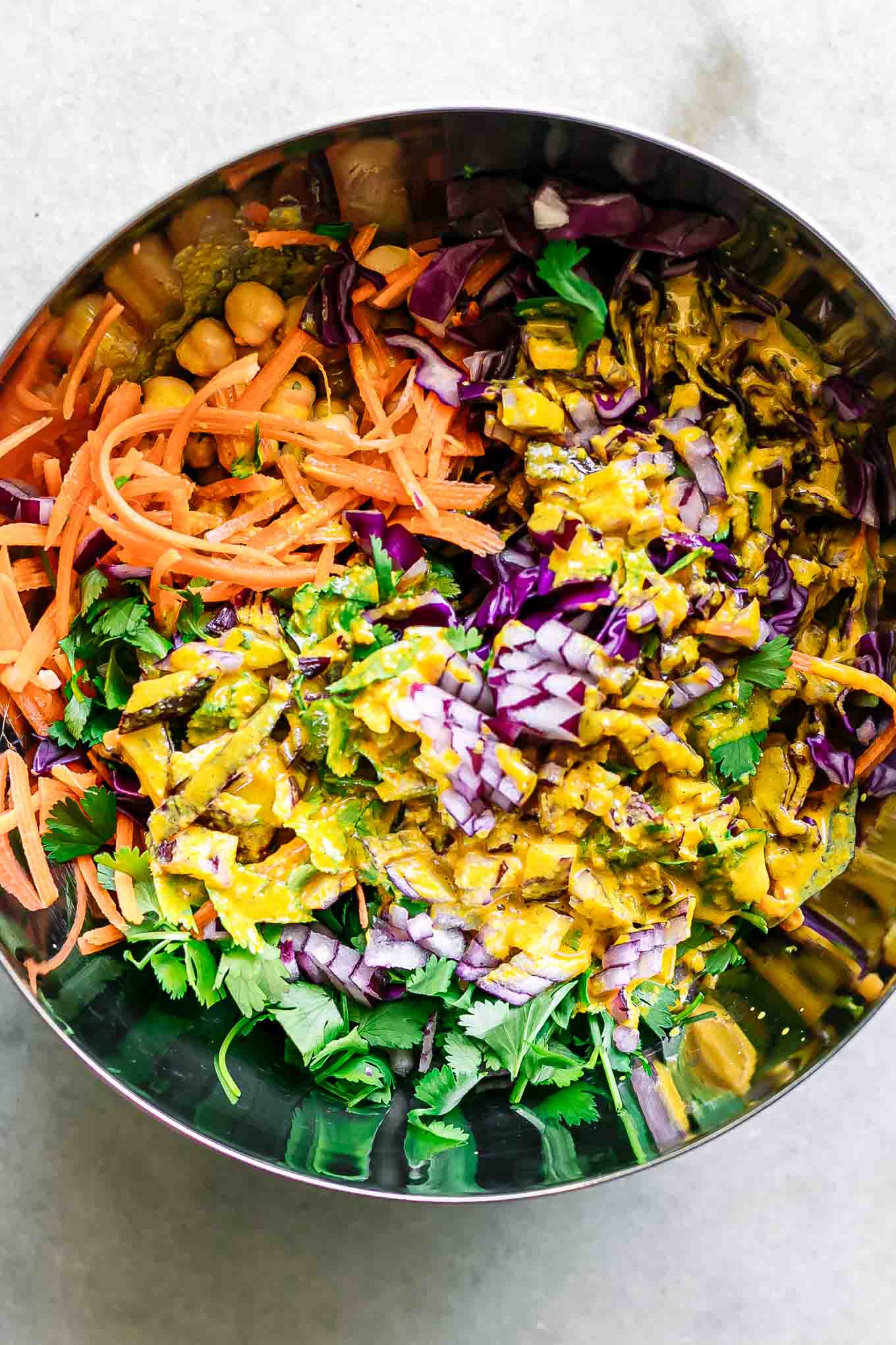 a metal bowl with chickpeas, carrots, cilantro, quinoa, cabbage, red onions, and tahini sauce