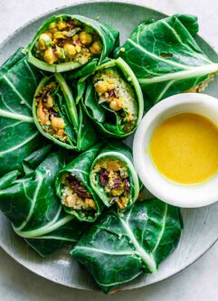 collard greens wraps stuffed with chickpea quinoa salad on a plate with a bowl of yellow sauce