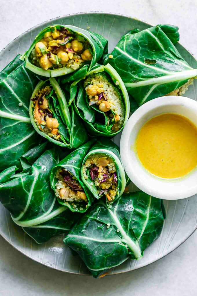 collard greens wraps stuffed with chickpea quinoa salad on a plate with a bowl of yellow sauce