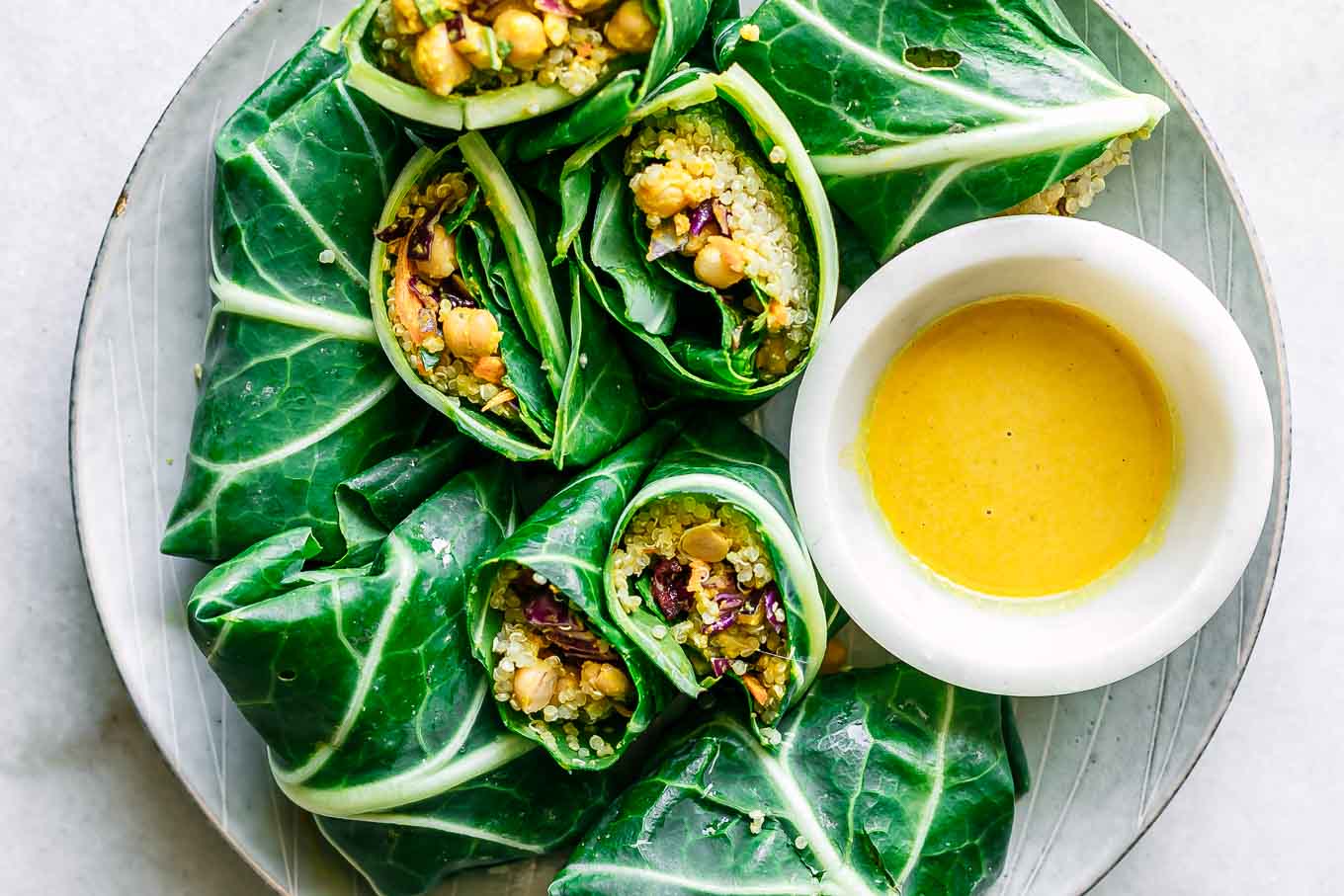 collard greens wraps with chickpea quinoa tahini curry salad on a white plate on a white table