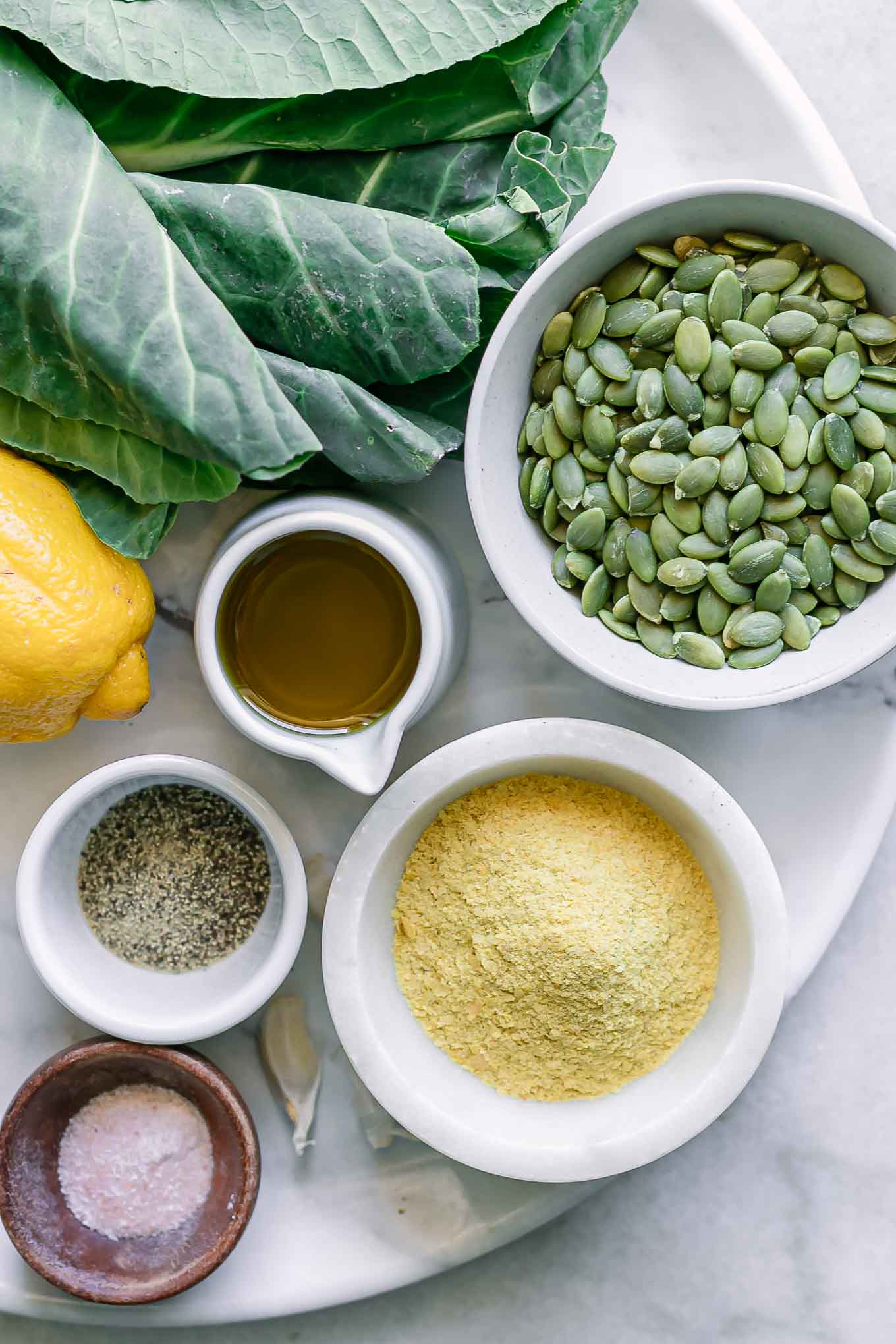 collard grens, bowls of pumpkin seeds, cheese, oil, lemon, salt, and pepper for pesto on a white table