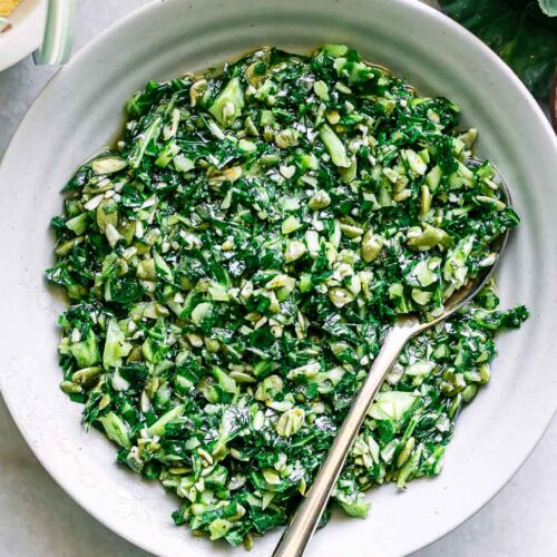 a bowl of collard greens pesto sauce on a white table with a gold spoon