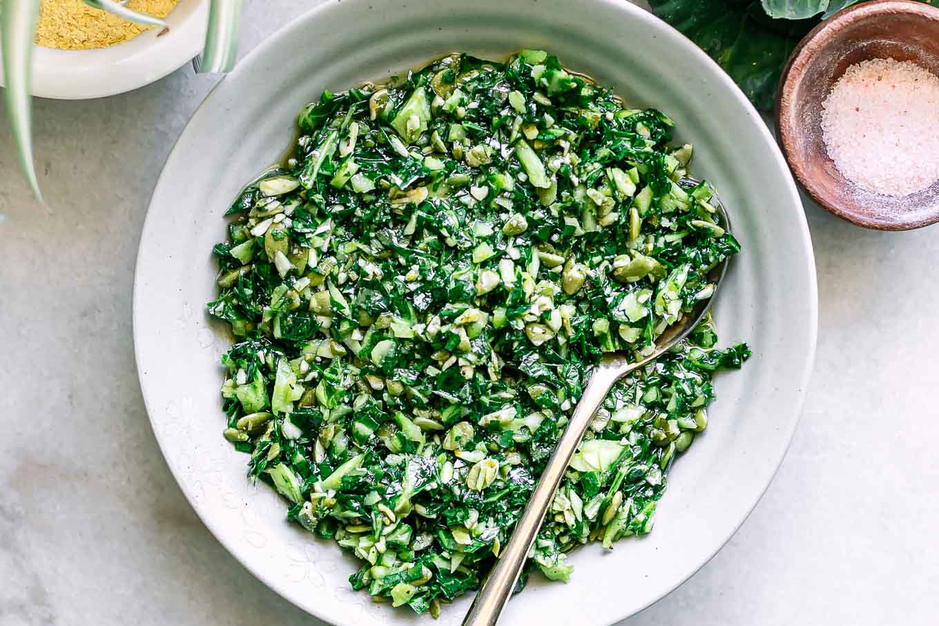 a bowl of collard greens pesto sauce on a white table with a gold spoon