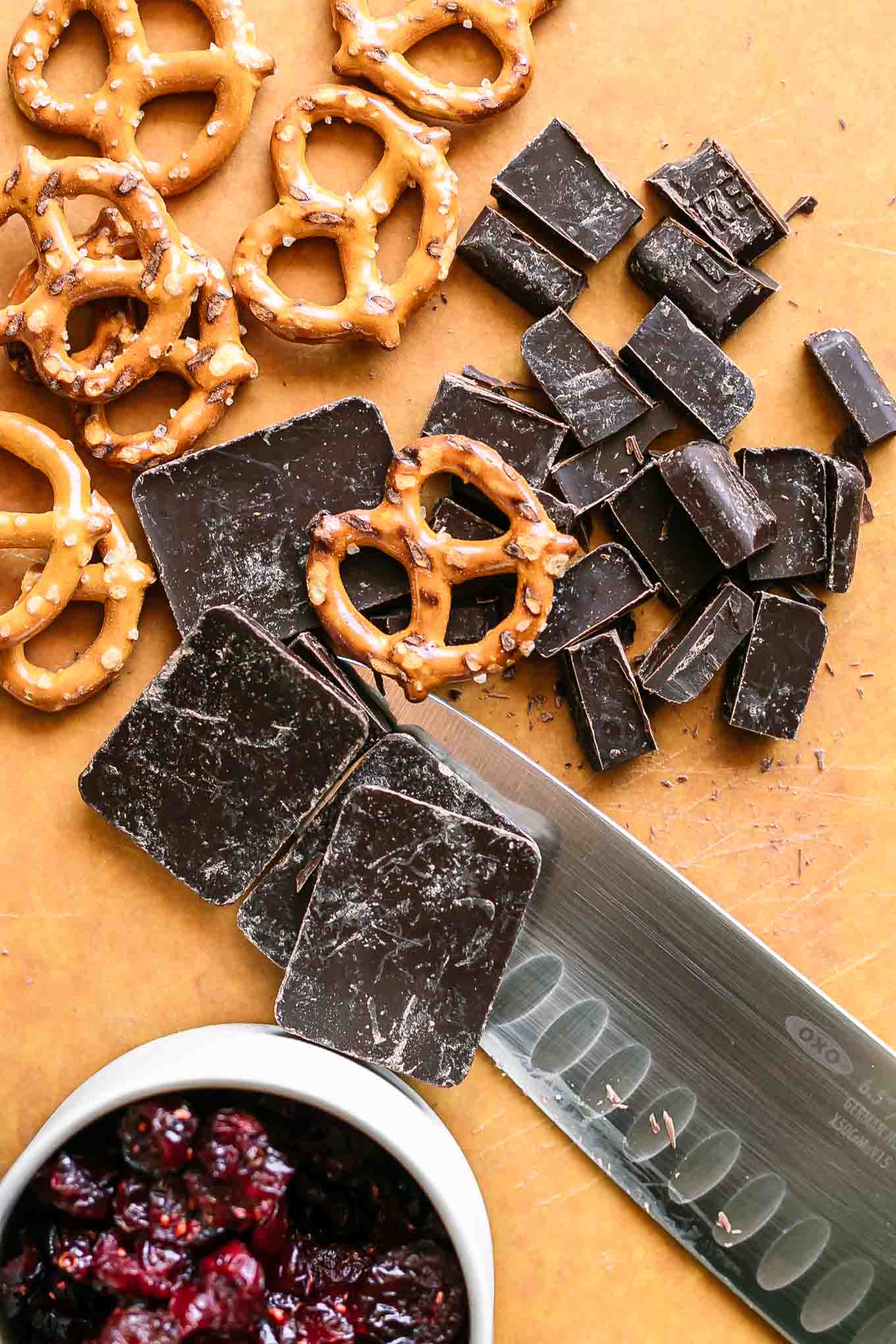 pretzels, dark chocolate, and dried cranberries on a cutting board with a knife