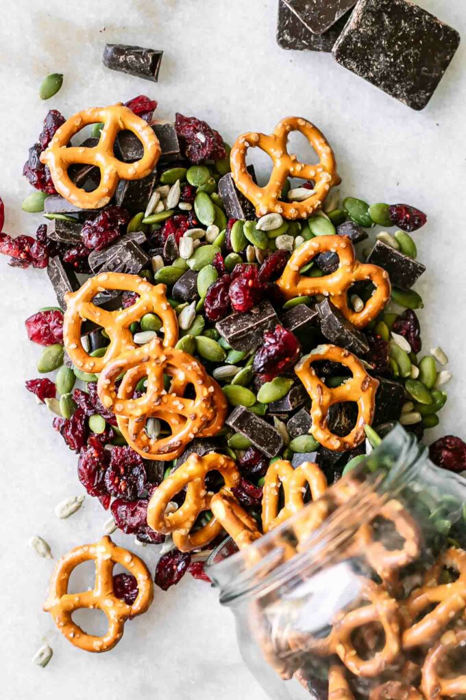 trail mix with pretzels, dark chocolate, dried cranberries, and pumpkin and sunflower seeds on a white table