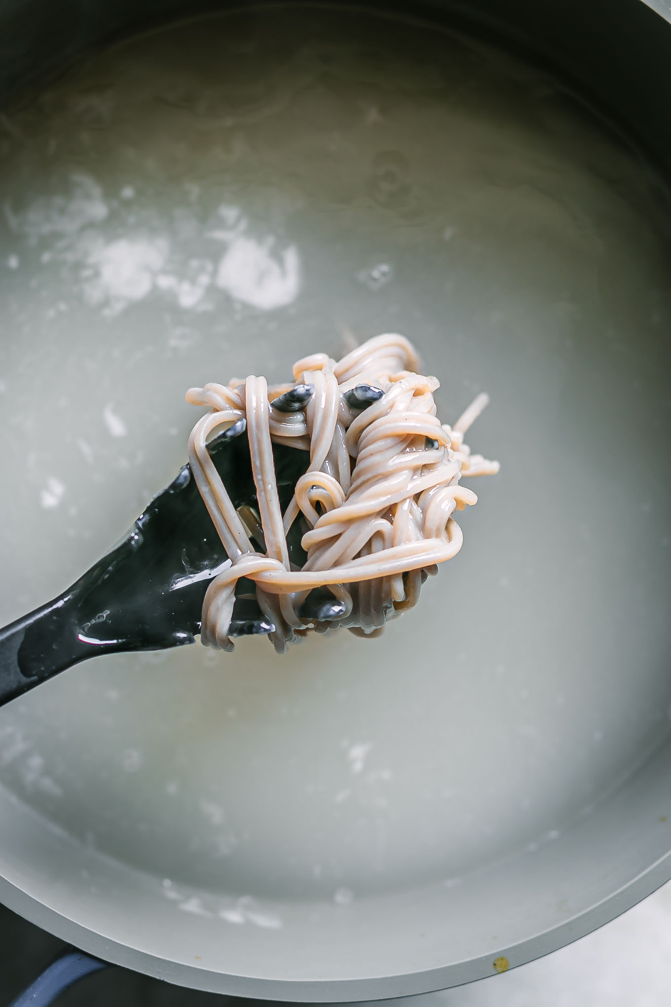 a black spaghetti fork with soba noodles over a pot of boiling water