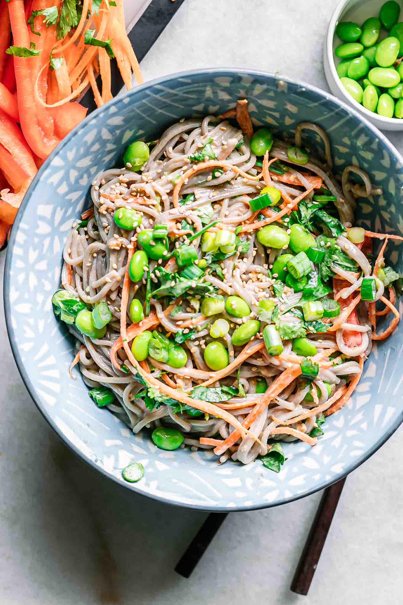 a bowl of soba noodle salad with edamame on a white table
