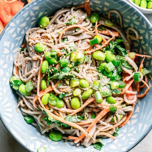 a blue bowl with sesame ginger soba noodle salad on a white table