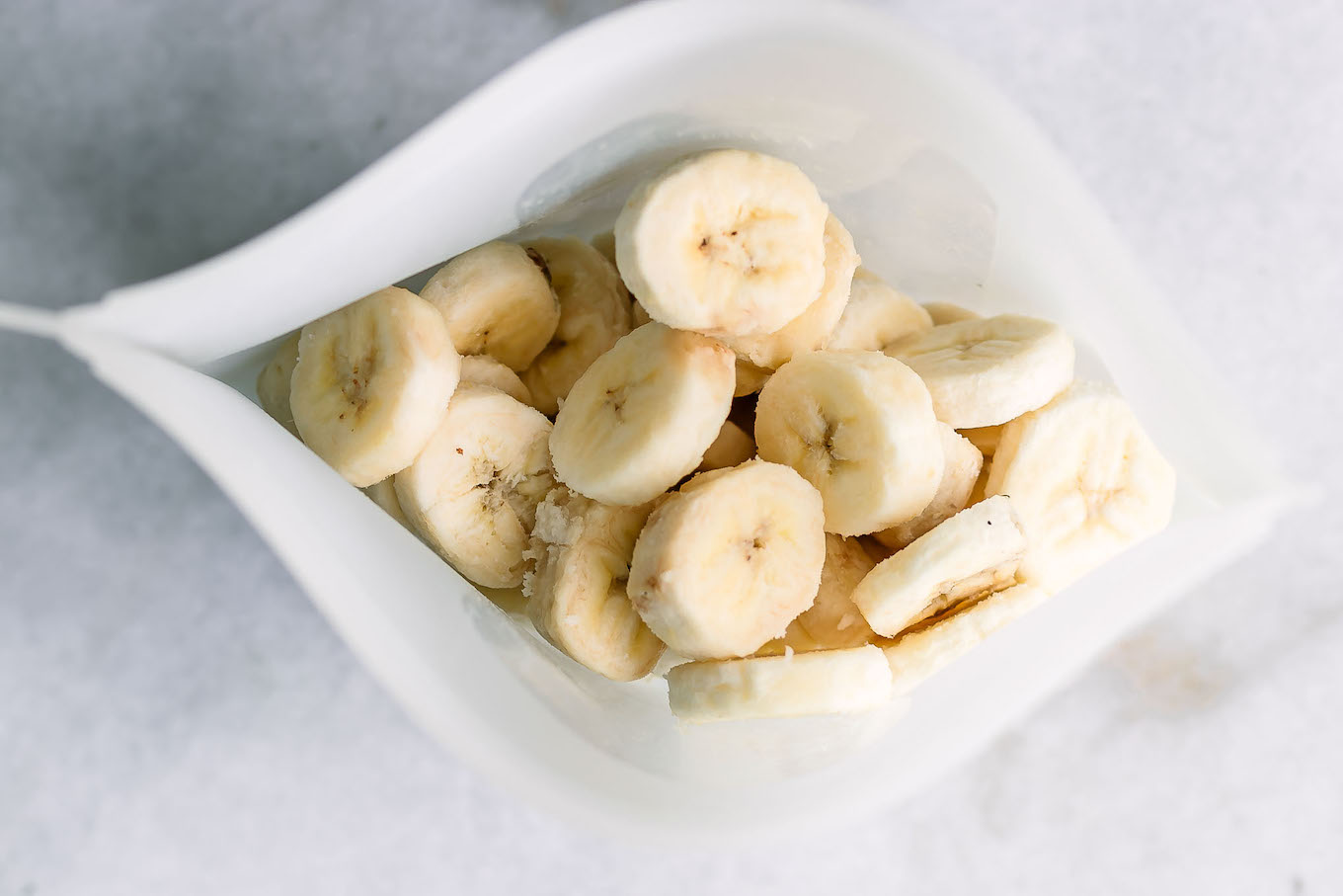 a freezer bag with frozen banana slices on a white table