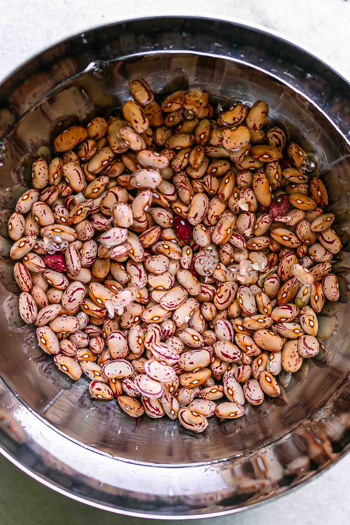 a metal bowl with cranberry beans soaking in water on a white table