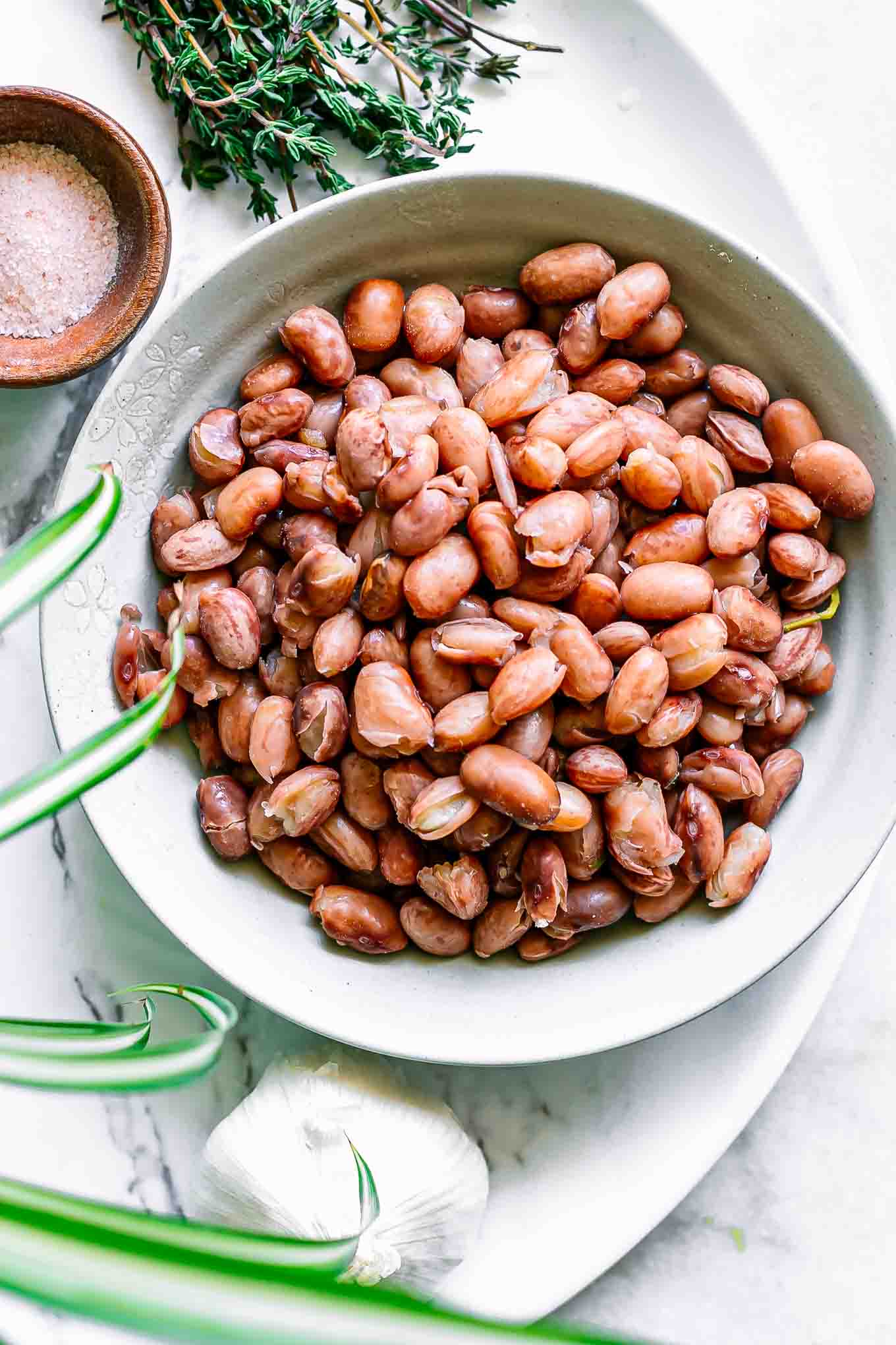 a bowl of cooked cranberry beans on a white table with herbs and spices