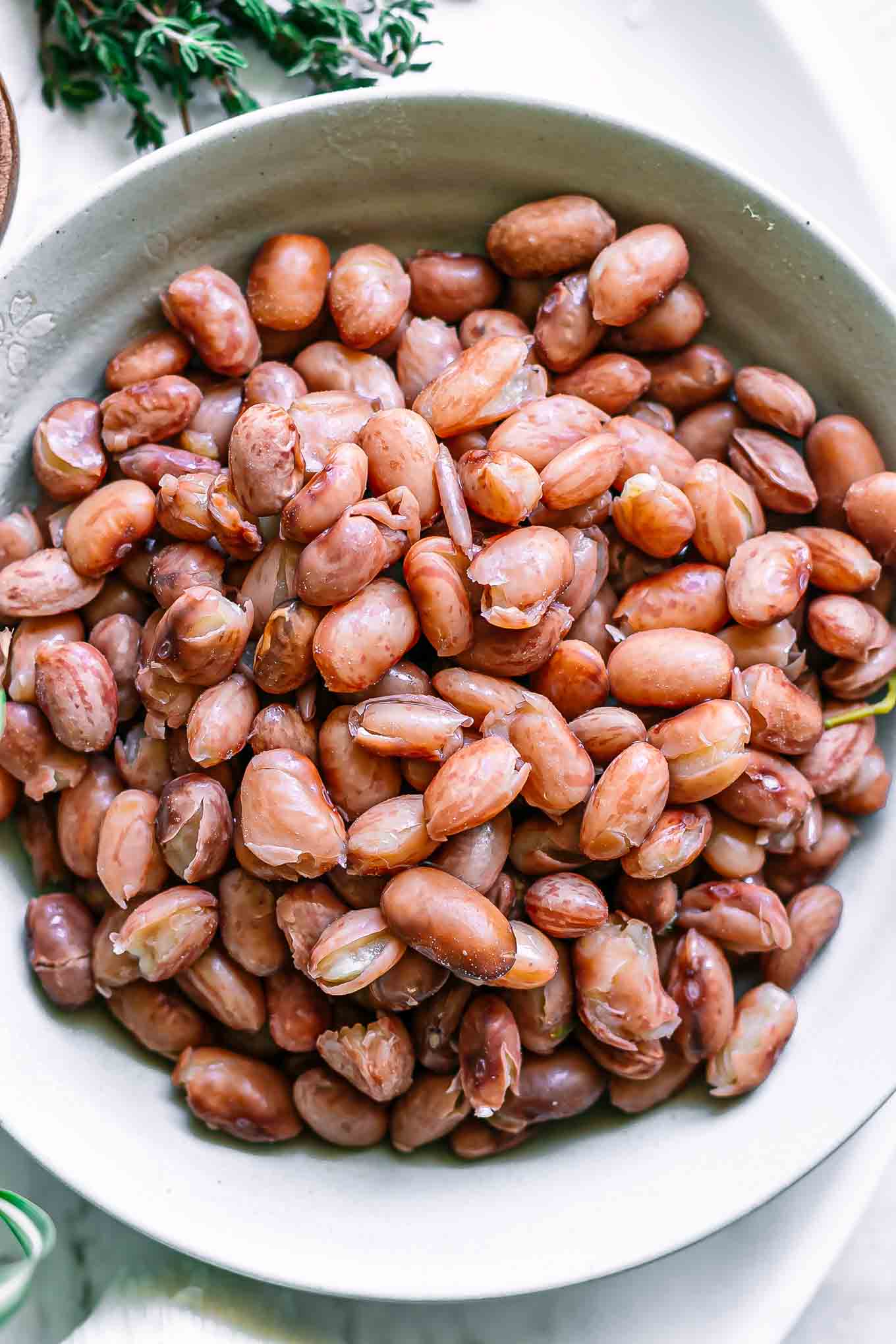 a close up photo of cooked borlotti beans in a bowl on a white table