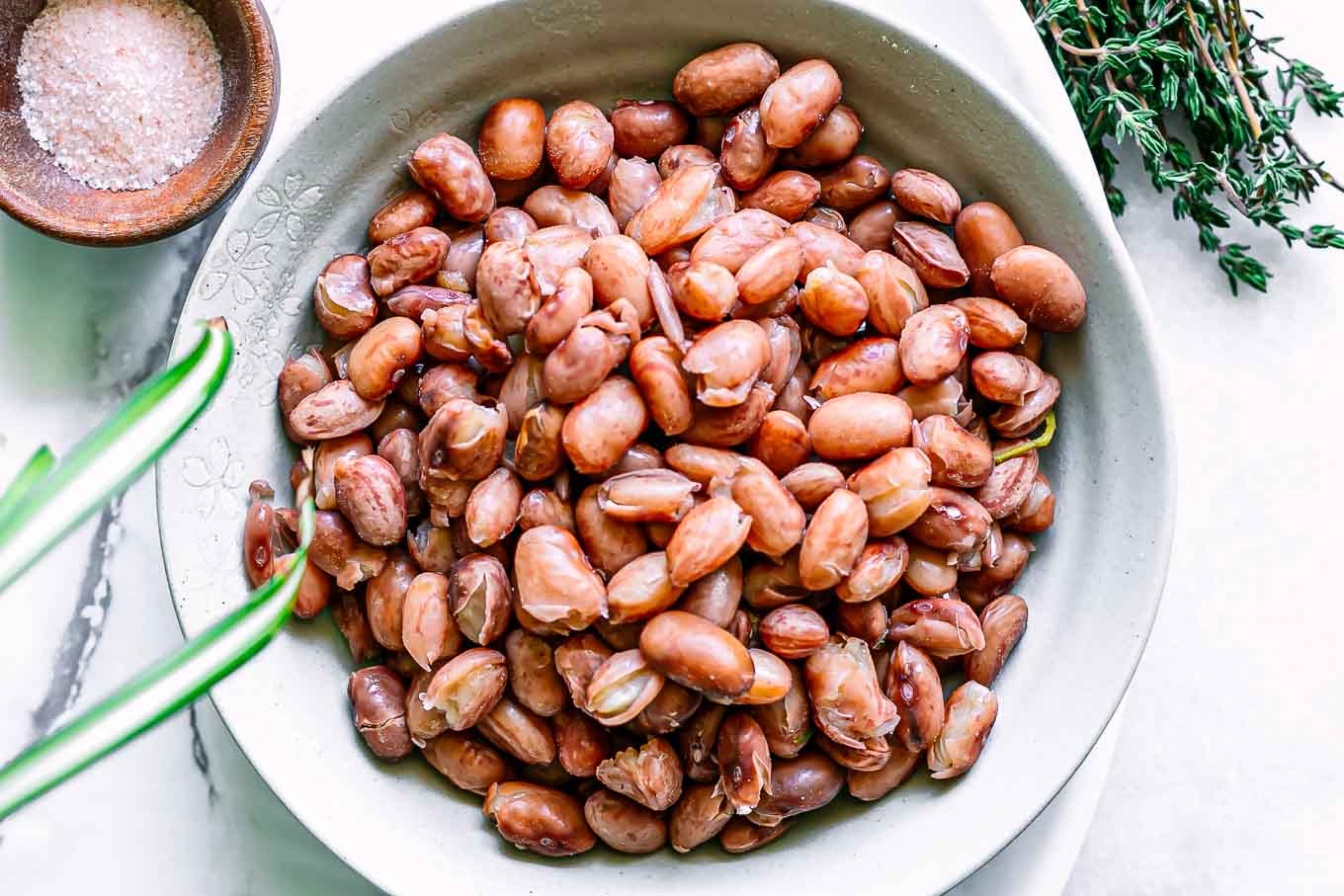 a bowl of cooked cranberry beans on a white table with bowls of spices and herbs