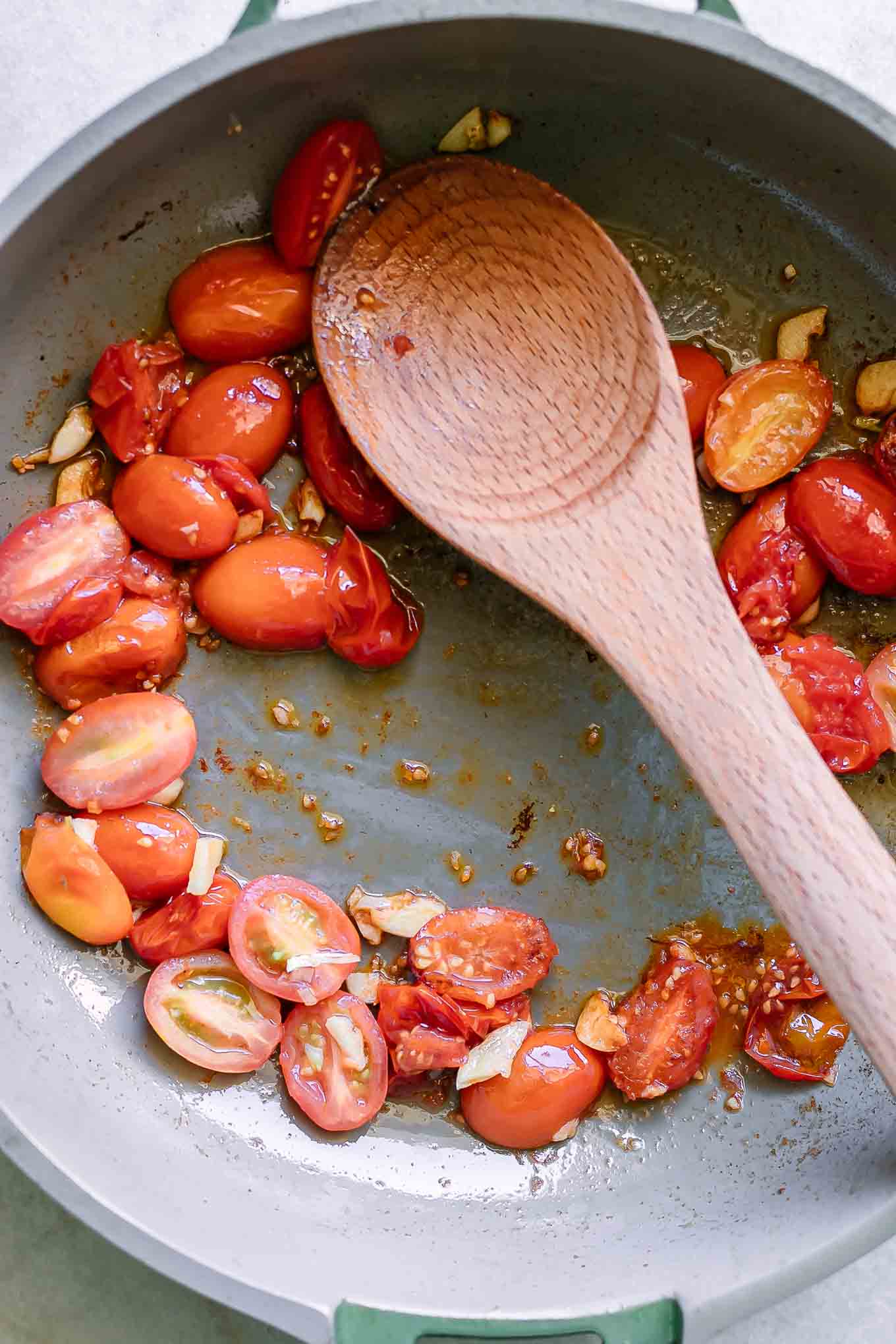a pan with burst cherry tomatoes and a wood spoon