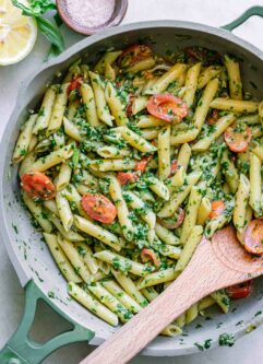 a pan with pesto penne pasta with a wooden spoon on a white table