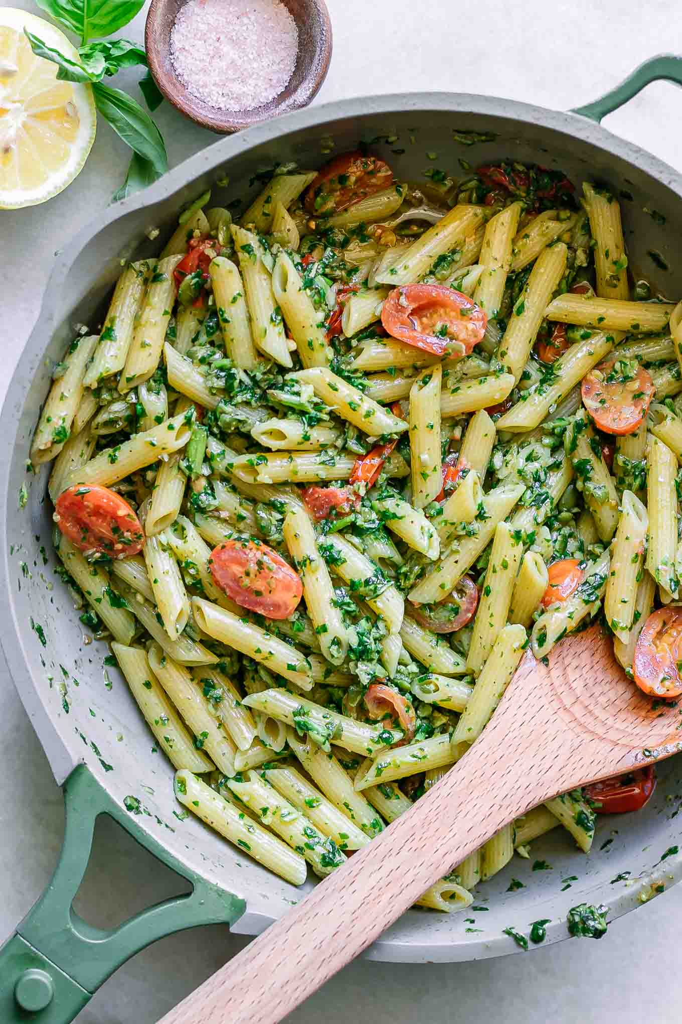 a pan with pesto penne pasta with a wooden spoon on a white table