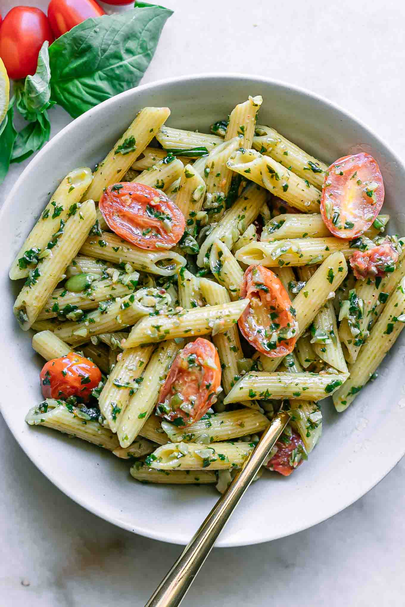 a bowl with pesto penne pasta with cherry tomatoes on a white table