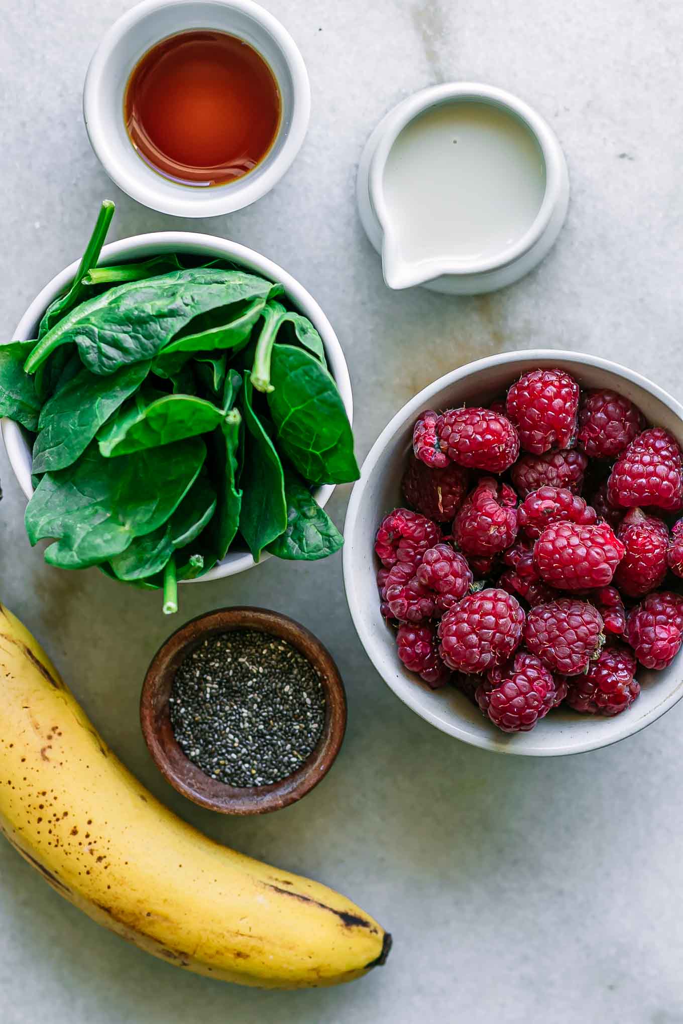 bowls of raspberries, spinach, milk, chia seeds, and bananas for a smoothie