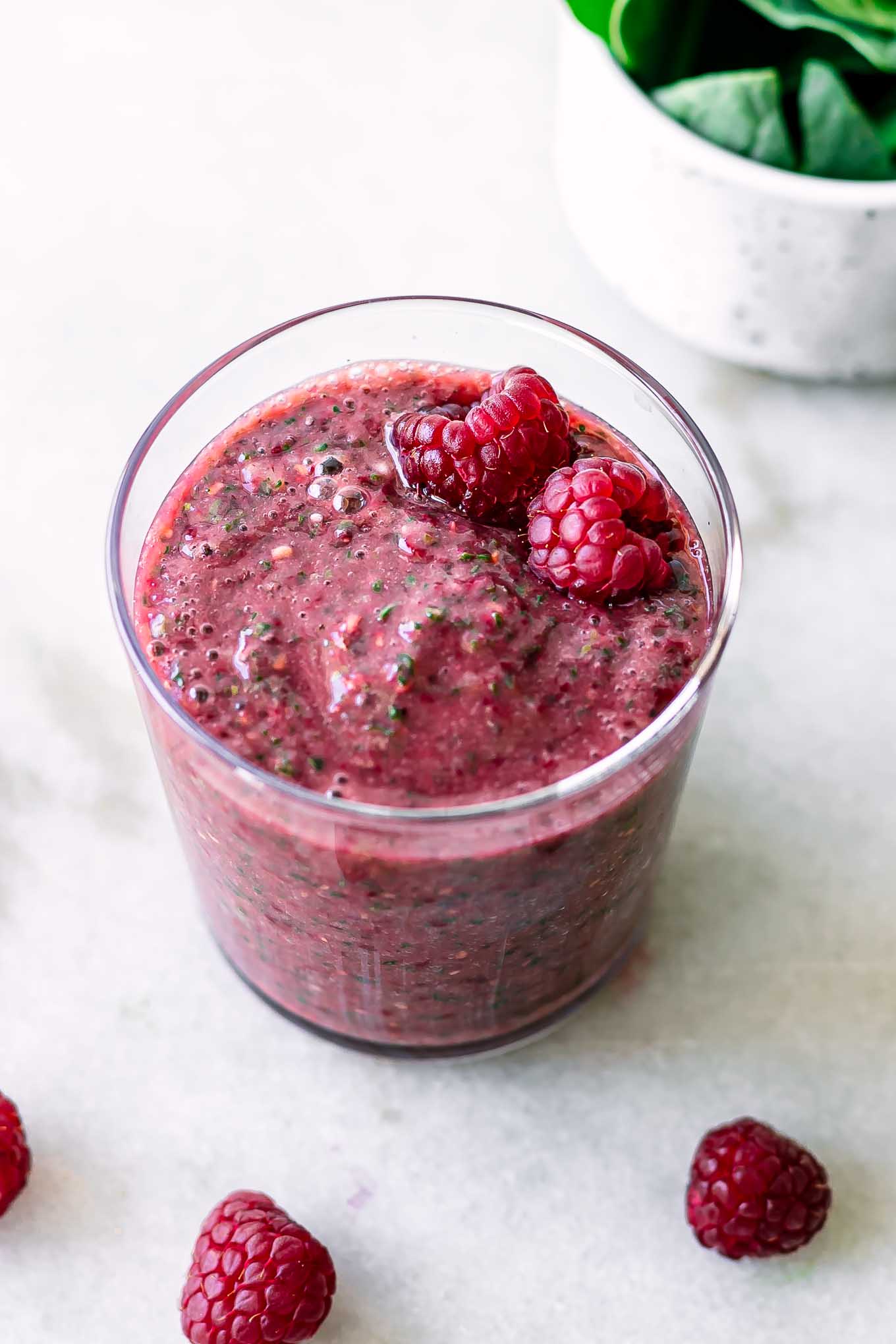 a raspberry spinach smoothie in a glass on a white table with fresh raspberries