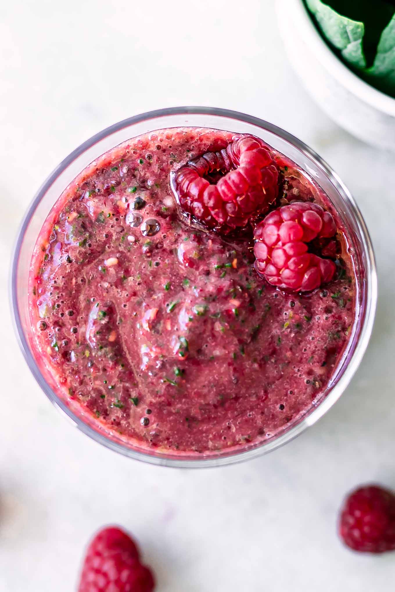 a close up of a raspberry and spinach smoothie with two raspberries on top
