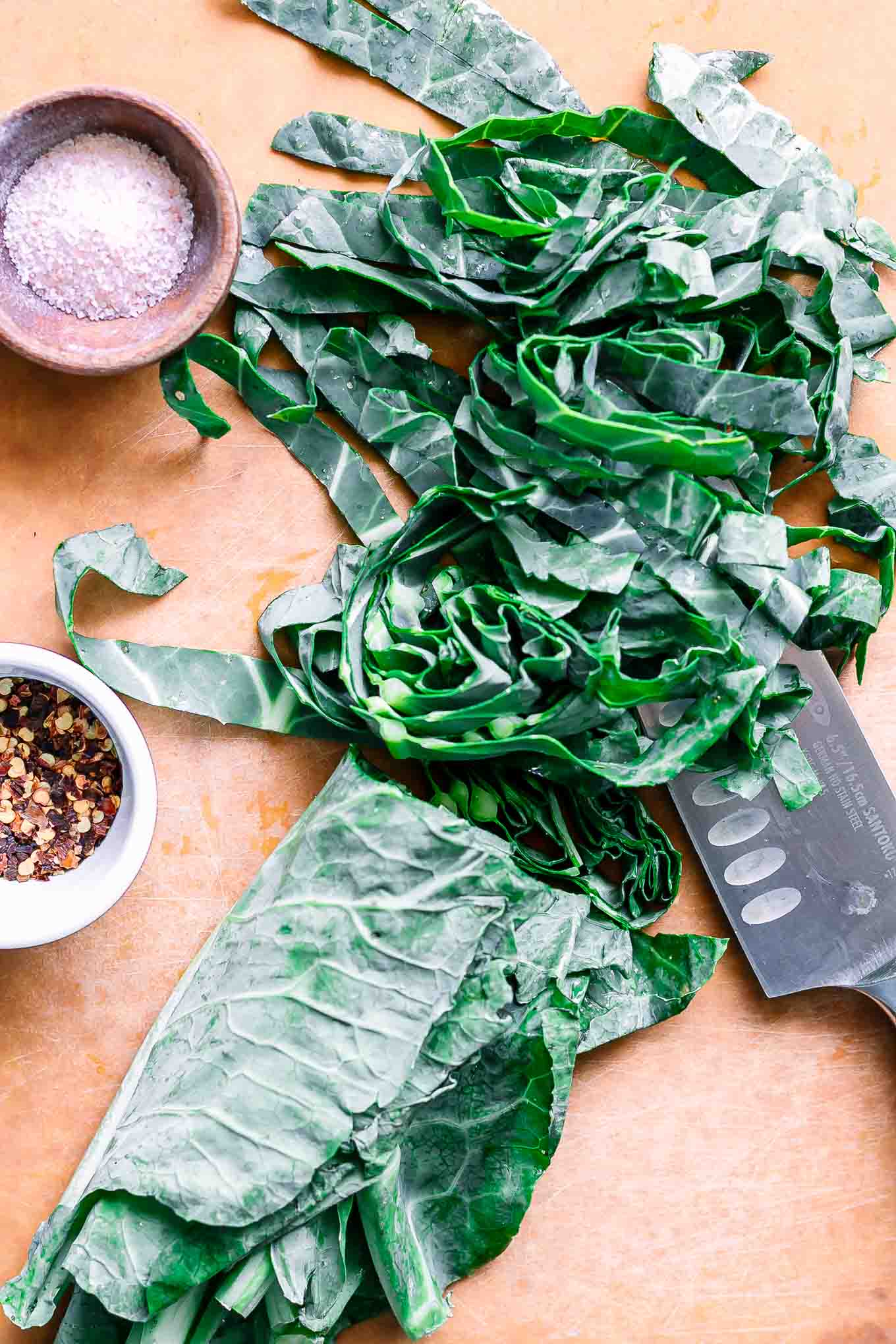 sliced collard greens on a wood cutting board with a knife